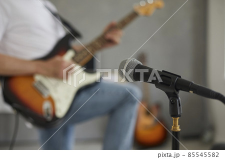 Close up of professional microphone in recording studio or rehearsal room on background of musician on blurred background. Selective focus. Soft. Concept of recording music in studio. 85545582