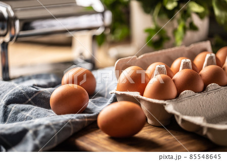 Fresh eggs in a cardboard box on a wooden board in the kitchen. 85548645