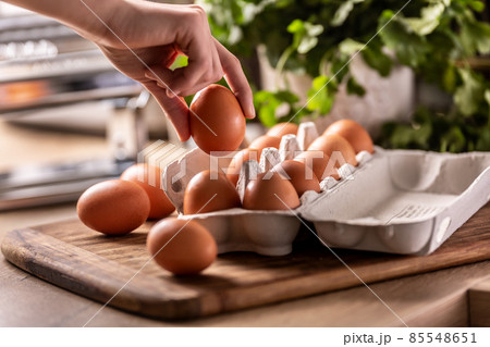 Female hand picks an egg with a carton box lying on the kitchen counter. 85548651