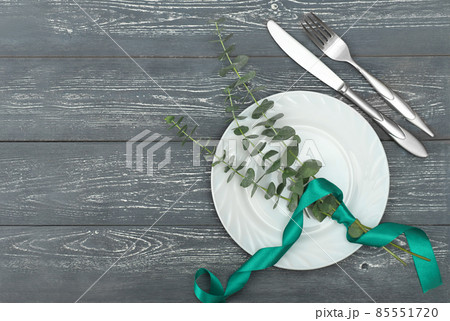 Spring elegant table setting, spring restaurant menu concept. top view of white dishes and silverware next to eucaliptus branches on a grey rustic table.  85551720