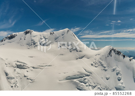 Minimalist view of snow-capped mountain wall in thick low clouds in sunshine. Scenic bright mountain landscape with white-snow peak among dense clouds in blue sky. Wonderful scenery with snowy top. 85552268