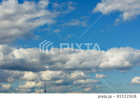 Lush white clouds cling to the top of the television tower's spire high above the blue sky. 85552938