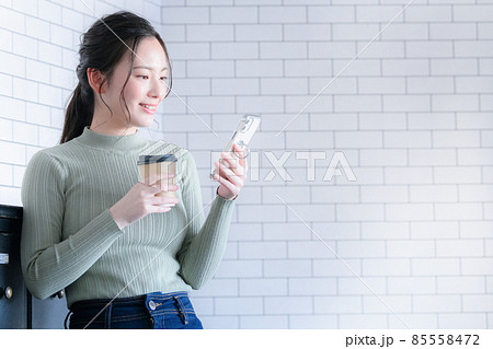 コーヒーを持ってスマホを検索する笑顔の女性 コピースペースあり コーヒーを持ってスマホを検索する笑顔の女性 コピースペースあり 85558472