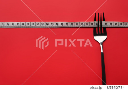 Loss weight and healthy diet concept. Fork with measuring tape on red background. Copy space for text. Loss weight and healthy diet concept. Fork with measuring tape on red background. Copy space for text. 85560734