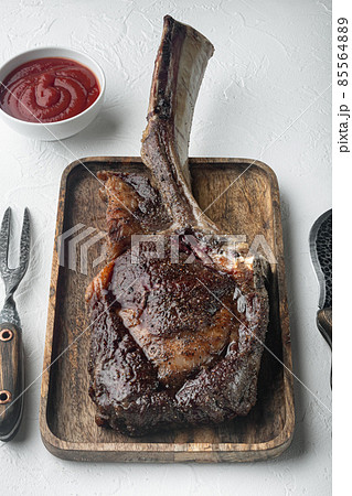 Steak on the bone. tomahawk steak freshly grilled dry aged BBQ food, on wooden serving board, on white stone background Steak on the bone. tomahawk steak freshly grilled dry aged BBQ food, on wooden serving board, on white stone background 85564889