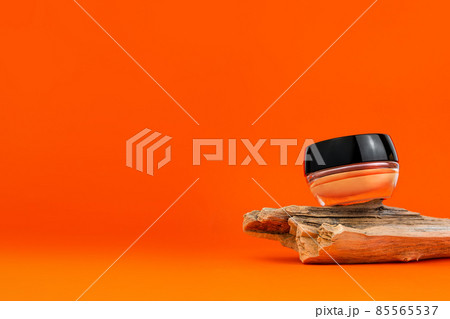 Cosmetic face BB cream tonal foundation glass jar mockup natural wood podium orange background. Balancing makeup product 85565537