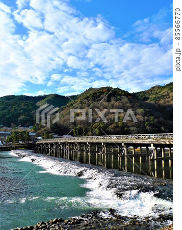 渡月橋、杭の間を川の流れの水流が流れ出ている、青空と白い雲、嵐山が写っている 渡月橋、杭の間を川の流れの水流が流れ出ている、青空と白い雲、嵐山が写っている 85566770