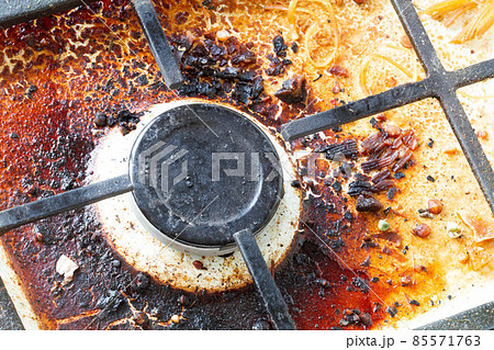 Dirty gas stove surface. Gas gas burner and cast iron grate of a gas oven surrounded by old leftovers of food and drinks. Top area surface and burner heads needs cleaning from burnt-on grease. Dirty gas stove surface. Gas gas burner and cast iron grate of a gas oven surrounded by old leftovers of food and drinks. Top area surface and burner heads needs cleaning from burnt-on grease. 85571763