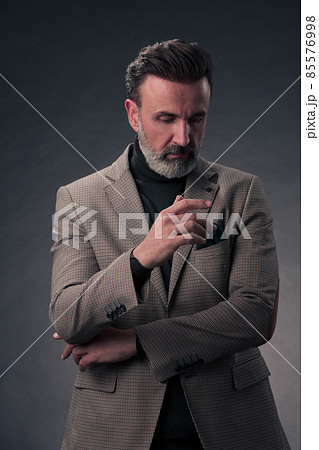 Portrait of a stylish elegant senior businessman with a beard and casual business clothes in photo studio isolated on dark background gesturing with hands 85576998
