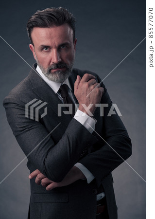Portrait of a stylish elegant senior businessman with a beard and casual business clothes in photo studio isolated on dark background gesturing with hands 85577070