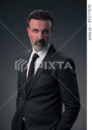 Portrait of a stylish elegant senior businessman with a beard and casual business clothes in photo studio isolated on dark background gesturing with hands Portrait of a stylish elegant senior businessman with a beard and casual business clothes in photo studio isolated on dark background gesturing with hands 85577076