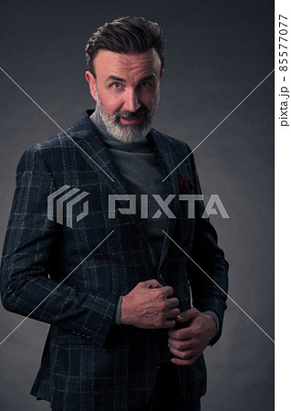Portrait of a stylish elegant senior businessman with a beard and casual business clothes in photo studio isolated on dark background gesturing with hands 85577077