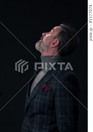 Portrait of a stylish elegant senior businessman with a beard and casual business clothes in photo studio isolated on dark background gesturing with hands 85577078