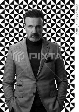 Black and white portrait of a stylish elegant senior businessman with a beard and casual business clothes against retro colorful pattern design background gesturing with hands Black and white portrait of a stylish elegant senior businessman with a beard and casual business clothes against retro colorful pattern design background gesturing with hands 85577082