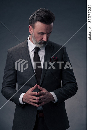 Portrait of a stylish elegant senior businessman with a beard and casual business clothes in photo studio isolated on dark background gesturing with hands 85577084
