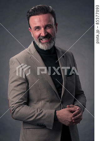 Portrait of a stylish elegant senior businessman with a beard and casual business clothes in photo studio isolated on dark background gesturing with hands 85577093