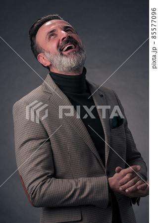 Portrait of a stylish elegant senior businessman with a beard and casual business clothes in photo studio isolated on dark background gesturing with hands 85577096