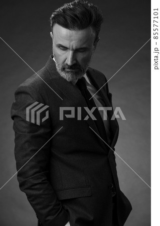 Portrait of a stylish elegant senior businessman with a beard and casual business clothes in photo studio isolated on dark background gesturing with hands Portrait of a stylish elegant senior businessman with a beard and casual business clothes in photo studio isolated on dark background gesturing with hands 85577101