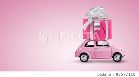 Pink toy car with gift box on a roof on pink background. Copy space. Pink toy car with gift box on a roof on pink background. Copy space. 85577110
