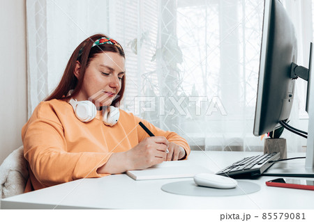 Caucasian woman student tired of learning doing homework using pc, woman studying preparing for exam test, writing in copybook doing literature research 85579081