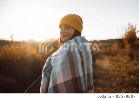 Outdoor woman with a blanket on her shoulders smiles enjoys sunset in autumn nature meadow at sunset in nature. Hope, mental strength concept. 85579087