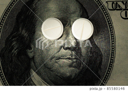 Covid-19 coronavirus pills lie instead of eyes on a one hundred dollar bill in close-up. The concept Covid-19 coronavirus pills lie instead of eyes on a one hundred dollar bill in close-up. The concept 85580146