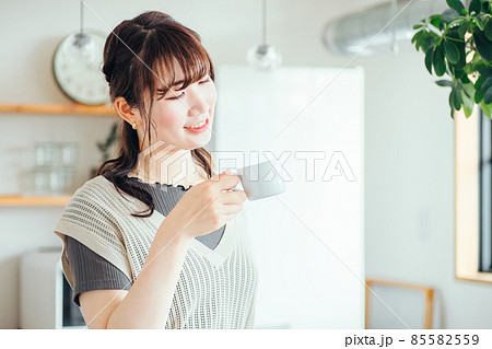 キッチンの前でホットドリンクを飲む女性 85582559