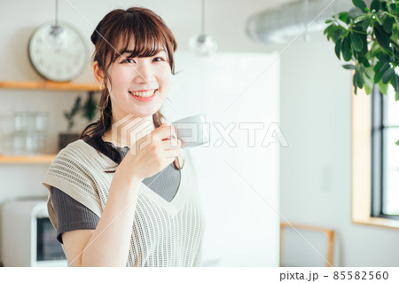キッチンの前でホットドリンクを飲む女性 85582560