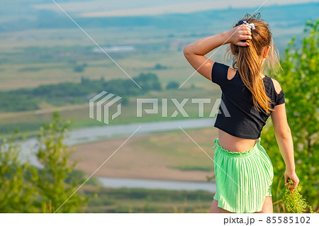 rear view. a child, a little girl stands on the top of a high hill, a mountain 85585102