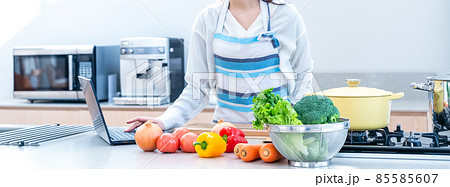 キッチンでノートパソコンの動画を見ながら料理をする主婦のイメージカット 85585607