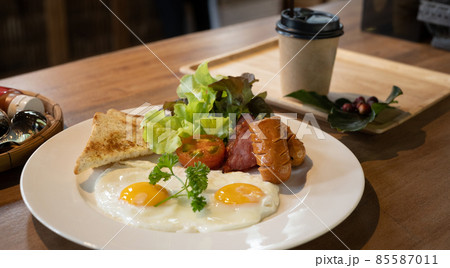 Fried eggs, bacon, sausages, toasts and fresh salad for breakfast. 85587011