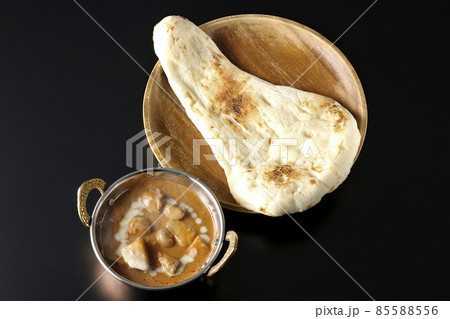 鶏肉や落花生など沢山の具材が入っている熱々マッサマンカレーとナンを黒背景で俯瞰撮影 85588556