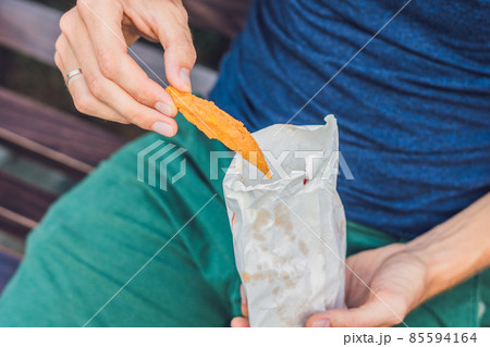 Man eat fried sweet potatoes in the park. Junk food concept Man eat fried sweet potatoes in the park. Junk food concept 85594164