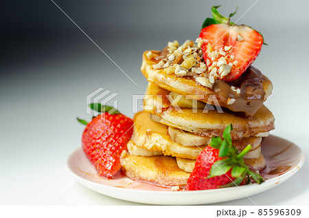 Pancakes stacked with bananas, strawberries and nuts, topped with chocolate and strawberry sauce 85596309