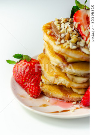 Pancakes stacked with bananas, strawberries and nuts, topped with chocolate and strawberry sauce 85596310