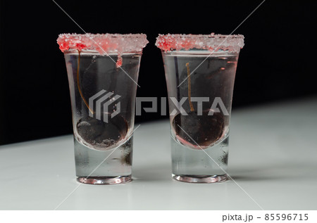 Drink  based on vodka, transparent cherry liqueur and syrup in drink shot glass, decorated with fresh cherry and red sugar 85596715