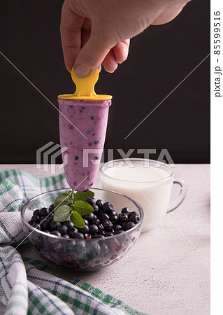 A woman's hand holds homemade ice cream with berries over a plate of blueberries on a dark background. The concept of cooking homemade food 85599516