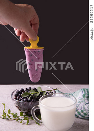 A woman's hand holds homemade ice cream with berries over a plate of blueberries. The concept of natural products 85599517