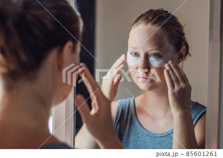 Portrait of Beauty Red-haired woman with eye patches showing an effect of perfect skin. Spa Girl Portrait of Beauty Red-haired woman with eye patches showing an effect of perfect skin. Spa Girl 85601261