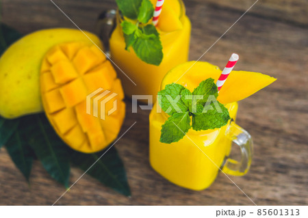 Juicy smoothie from mango in two glass mason jars with striped red straw on old wooden background. Healthy life concept, copy space 85601313