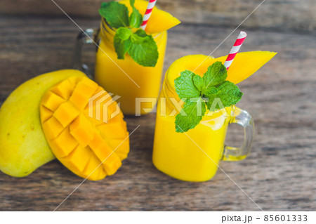Juicy smoothie from mango in two glass mason jars with striped red straw on old wooden background. Healthy life concept, copy space 85601333