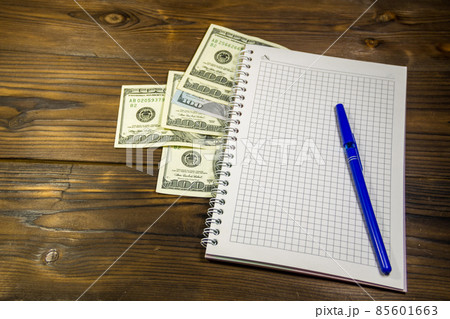 Notebook with ballpoint pen and dollar banknotes on the wooden desk 85601663