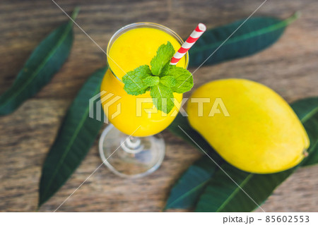 Juicy smoothie from mango in glass with striped red straw and with a mint leaf on old wooden background. Healthy life concept, copy space Juicy smoothie from mango in glass with striped red straw and with a mint leaf on old wooden background. Healthy life concept, copy space 85602553