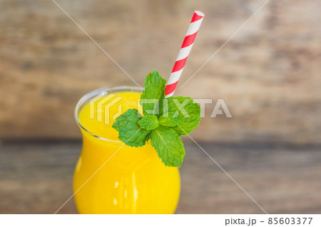 Juicy smoothie from mango in glass with striped red straw and with a mint leaf on old wooden background. Healthy life concept, copy space 85603377