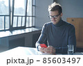 Handsome German businessman in eyewear sitting at desk at home office and using smartphone 85603497