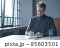 Confident focused German man freelancer in glasses taking notes in agenda sitting at desk at home 85603501