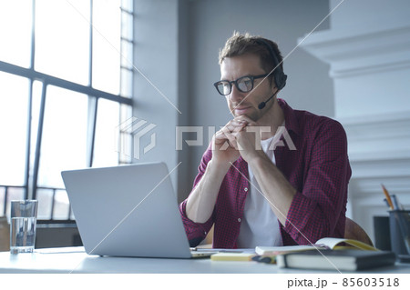 Pensive German businessman in headphones sits at desk while remotely working from home 85603518