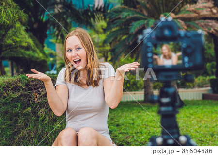 A young female blogger is leading her video blog in front of the camera in the park. Blogger concept 85604686