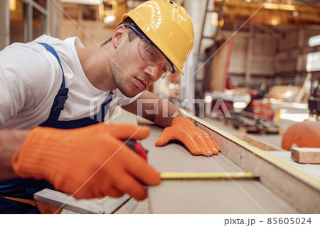 Serious man builder measuring wooden plank at construction site 85605024