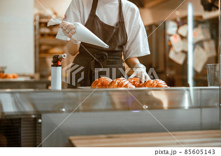 Lady holds sleeve with white cream ready to decorate croissants in bakery shop Lady holds sleeve with white cream ready to decorate croissants in bakery shop 85605143